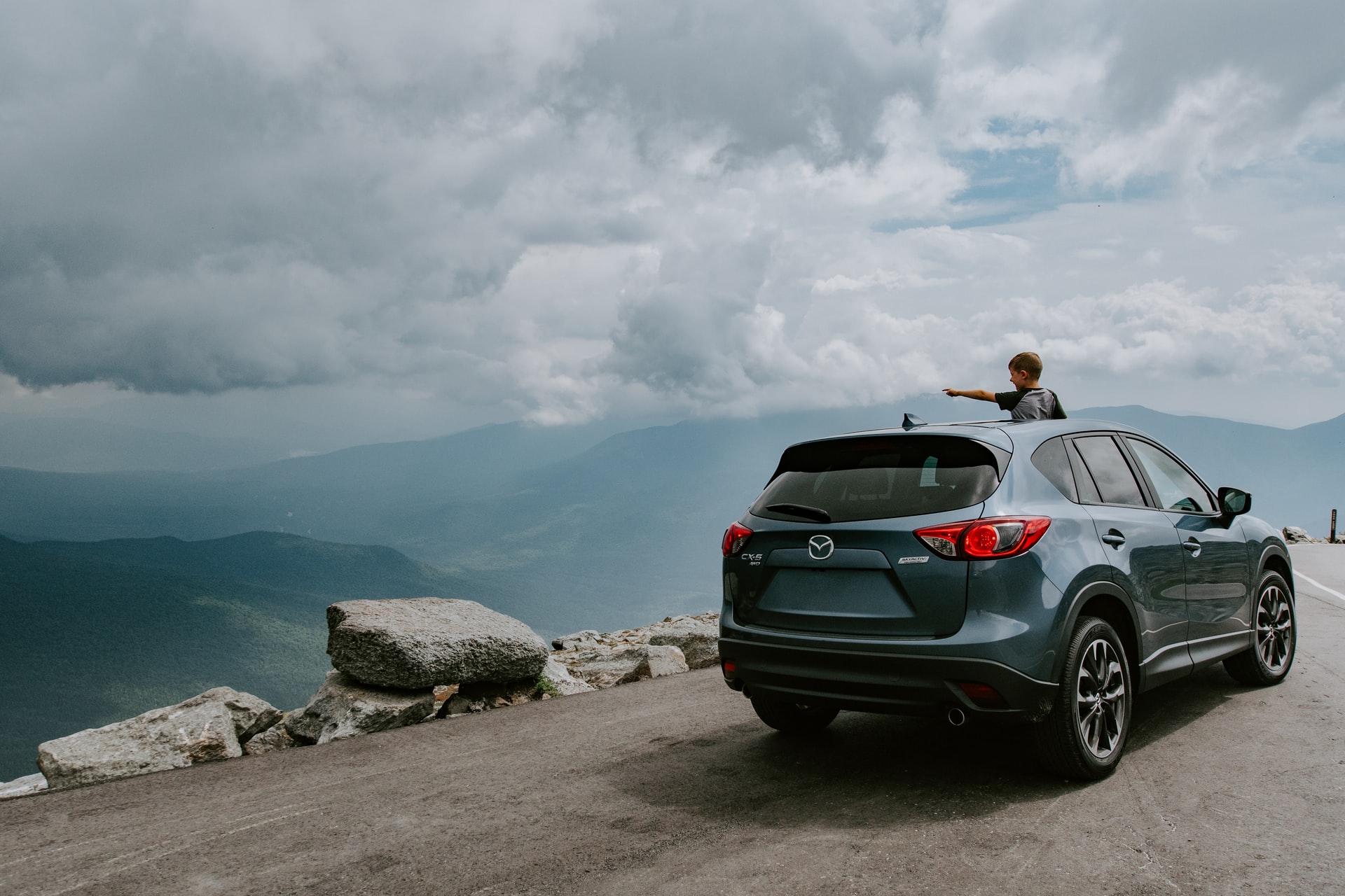 Boy standing through sub sunroof pointing at a view of the Applachian Mountains while on a road trip