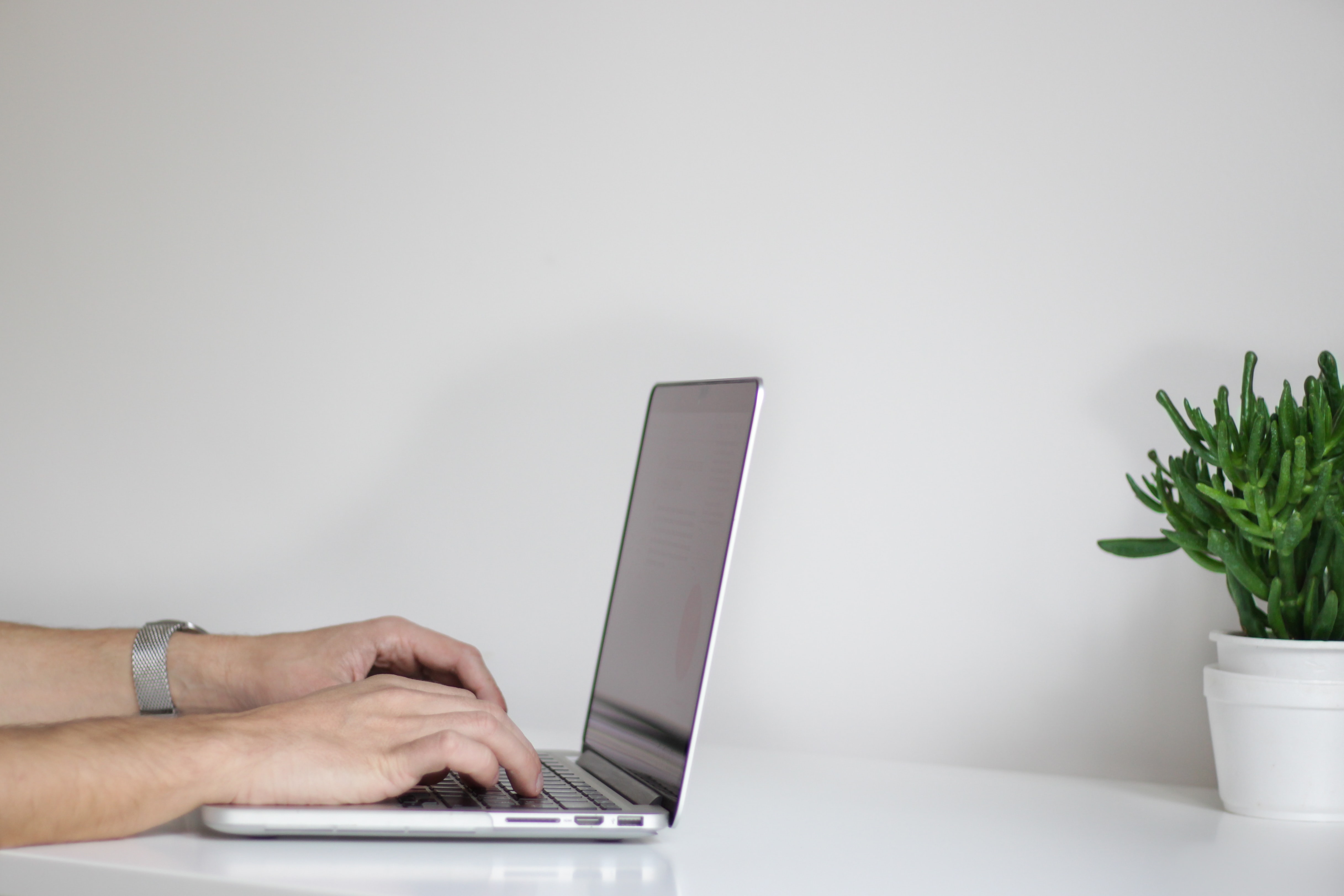 Side view of a laptop on a desk with hands on the keys